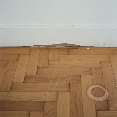 Detailaufnahme eines Parkettbodens mit feinen Kratzern und Wasserfleck an der Wand